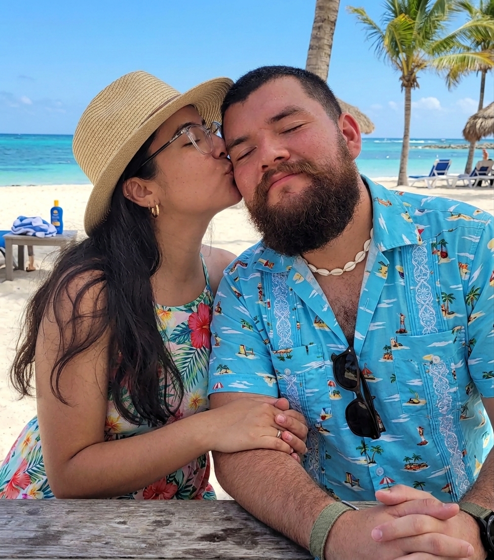 Lourdes y Nicolás sonriendo en la playa, con el mar turquesa de fondo